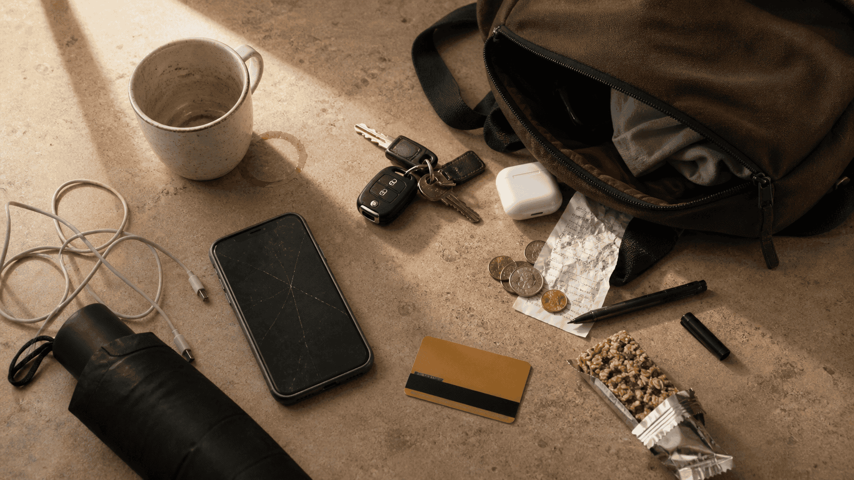 Scattered commuter items on counter — phone, keys, coffee mug with ring stain, crumpled receipt, loose change, open bag — daily micro stressors